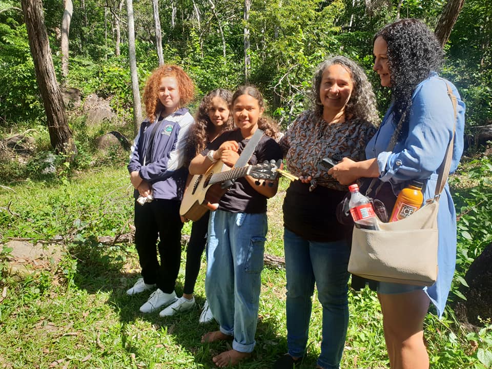 Group gathers in a forest clearing with a guitar