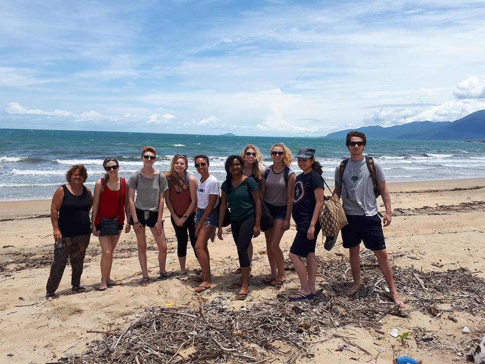 Travelers pose on a beach with mountains beyond