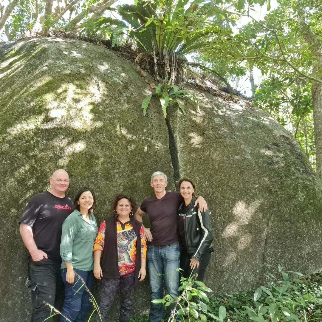 Visitors pose beside a giant forest boulder